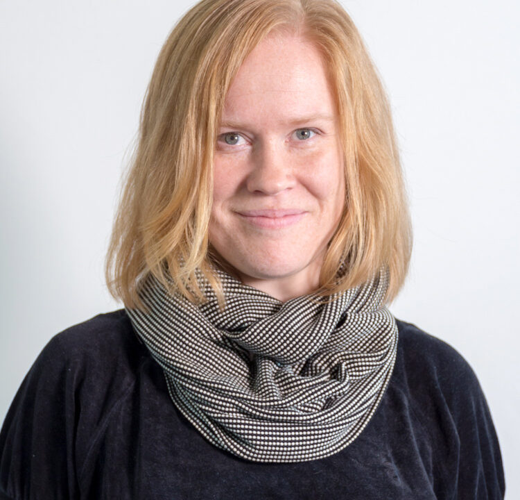 Vaaleahiuksinen nainen katsoo kohti hymynkare kasvoillaan.